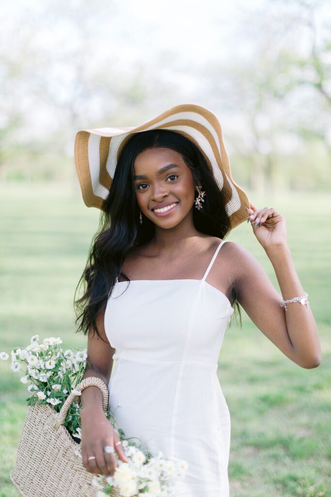 Senior portraits pose with hat and wildflowers in basket at park