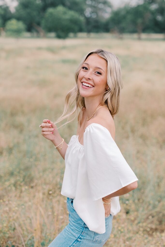 Senior girl in a field with soft light with natural, candid pose and smiling at camera.