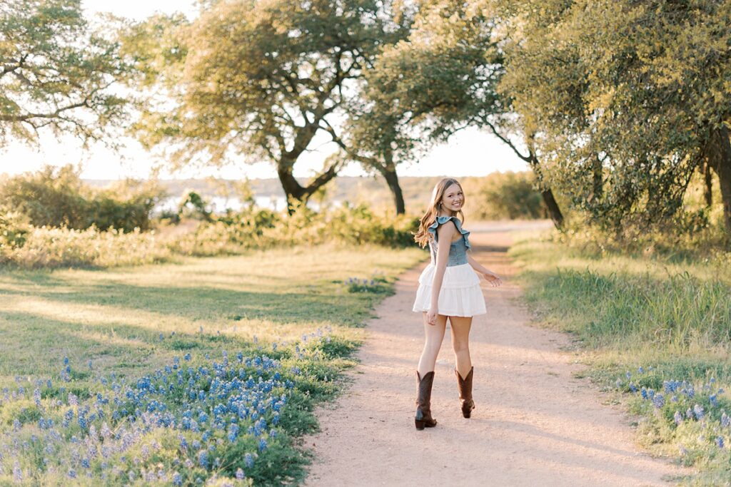 Senior photo of girl walking down trail during golden hour and looking back at the camera.