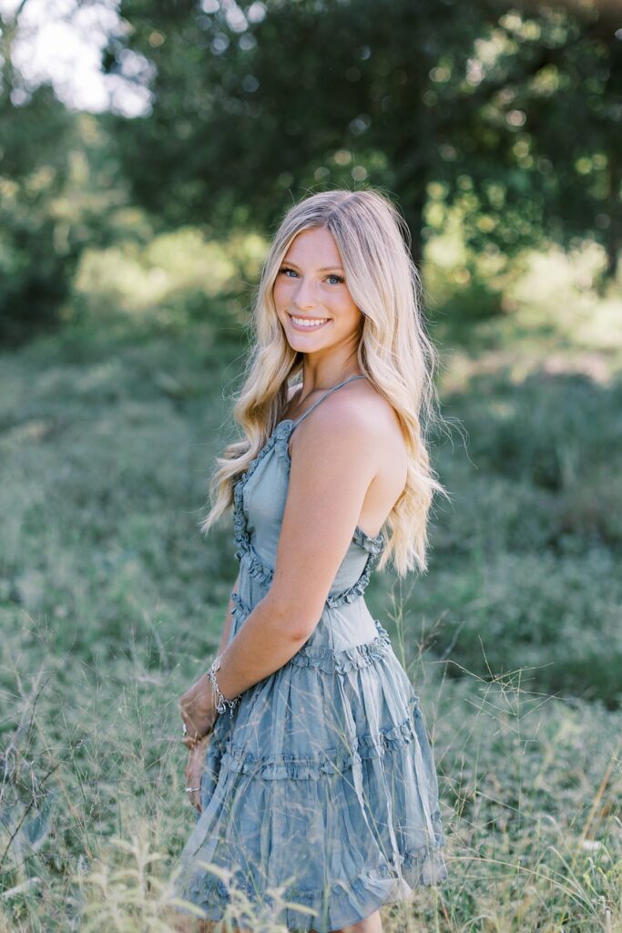 High school senior girl portrait relaxed and smiling in field at sunset