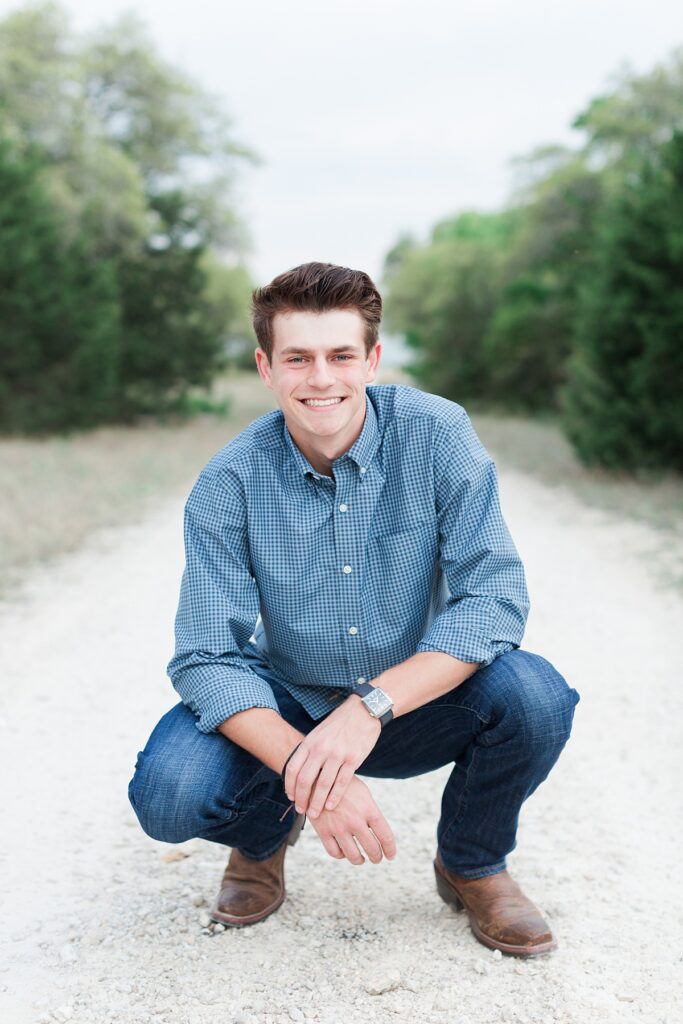 High school senior guy smiling and walking through a trail in grassy field in warm evening light