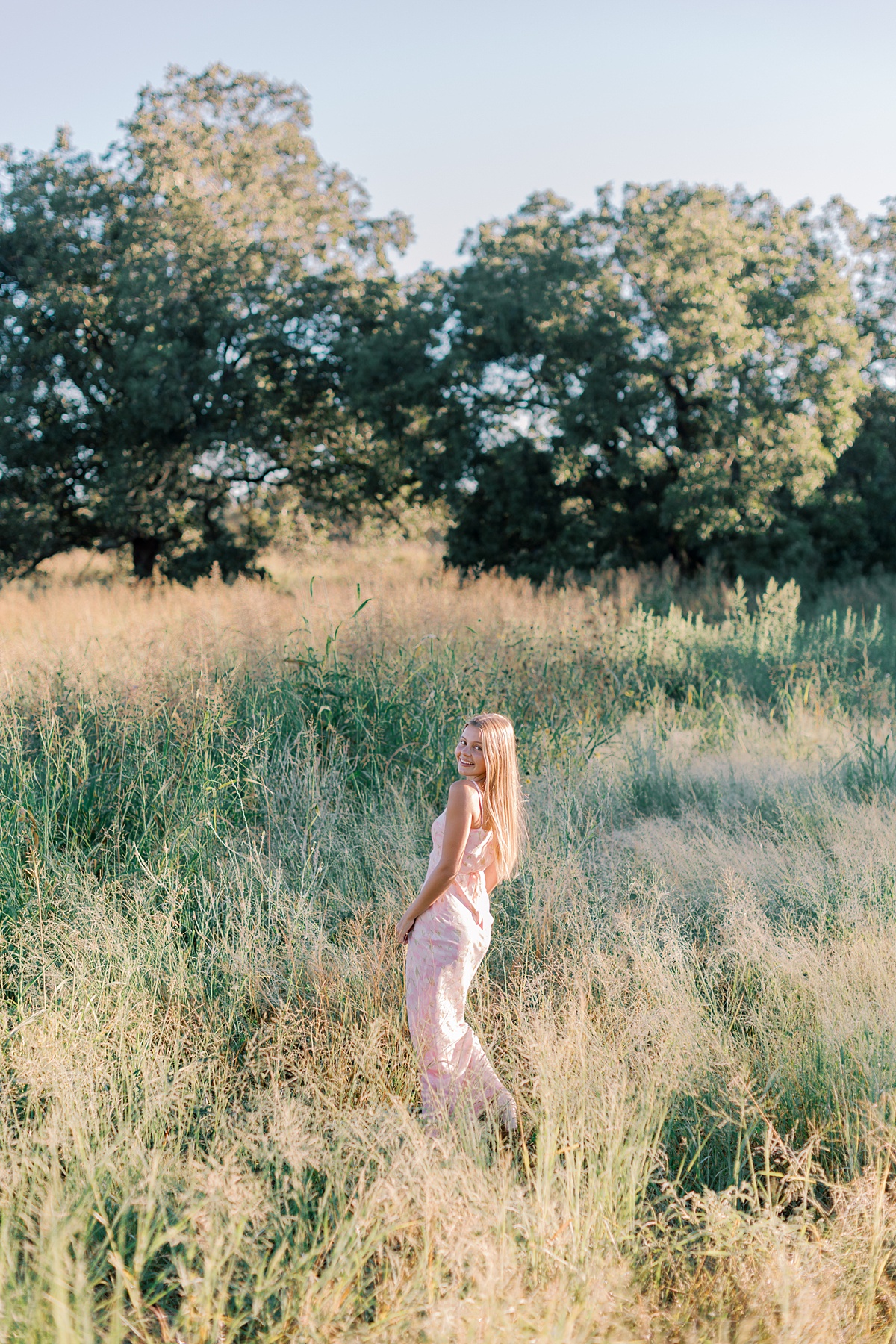 Senior girl twirling in a soft pink dress surrounded by tall grass in Malibu during her senior session