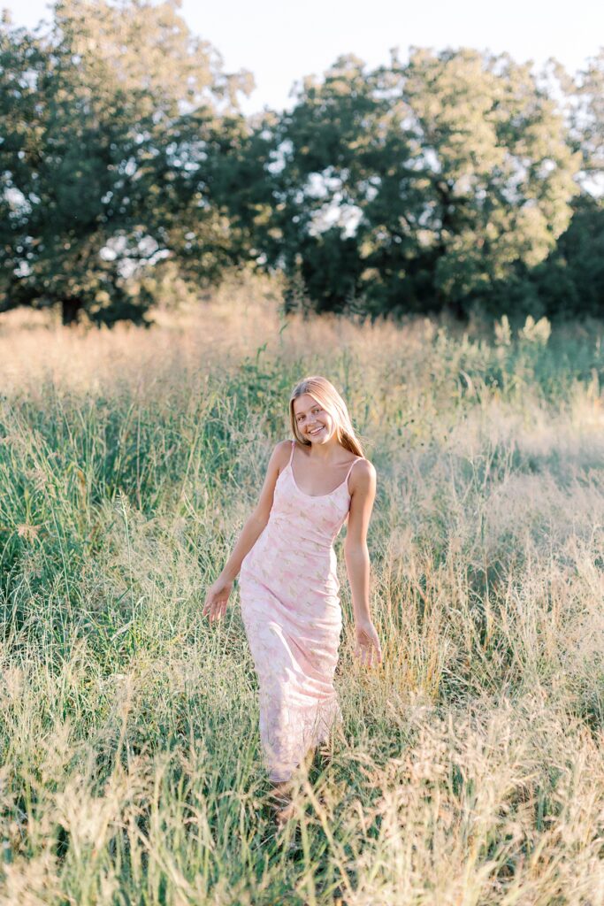 Senior girl walking through tall grass with golden light, showing outdoor senior photo ideas in Southern California