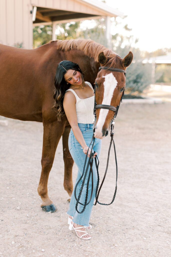 High school senior gently holding reins beside her horse – relaxed and confident equestrian portrait.