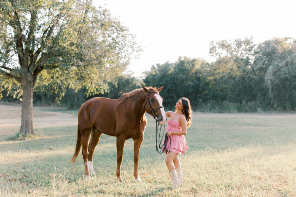 Natural portrait of a high school senior walking her horse through a pasture at sunset.