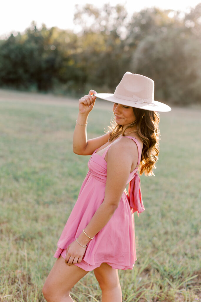 High school senior wearing a cowboy hat and pink dress in natural light – western style senior session inspiration.