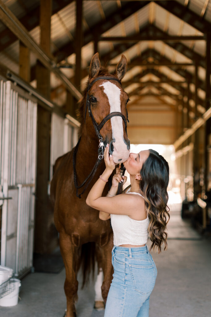 Close-up portrait of a high school senior kissing her horse inside the stable – authentic senior photos in Malibu.