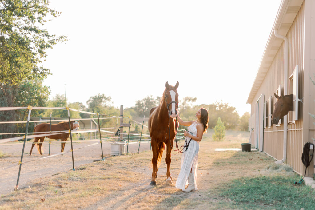 High school senior standing close to horse with soft light – warm equestrian image in field.