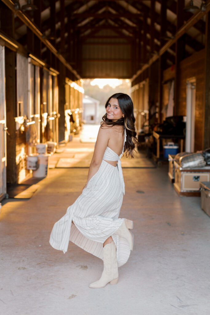 High school senior portrait of equestrian girl in long flowy dress with boots and golden hour light.