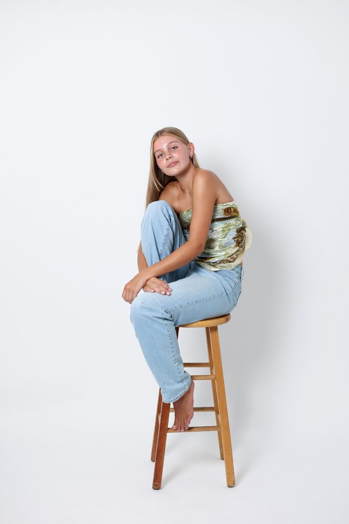 Creative Malibu senior studio photo of sitting sideways on a stool in light blue jeans