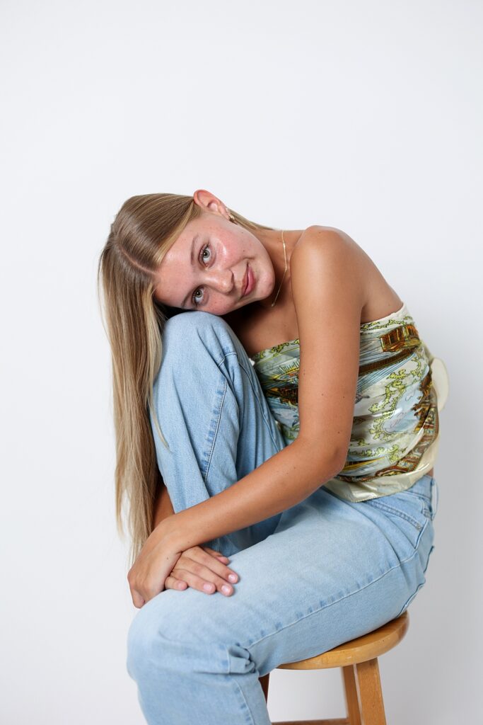 Relaxed senior picture of in a studio, resting her head on her knees with a soft smile