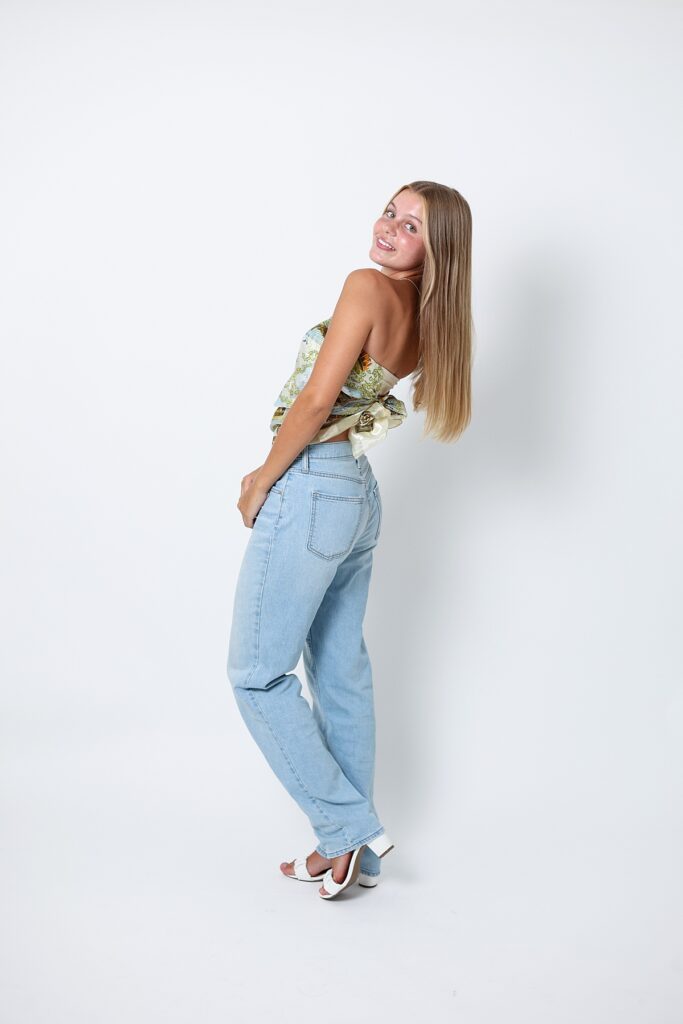 Full-length senior photo of in jeans and heels, posing in a Malibu studio