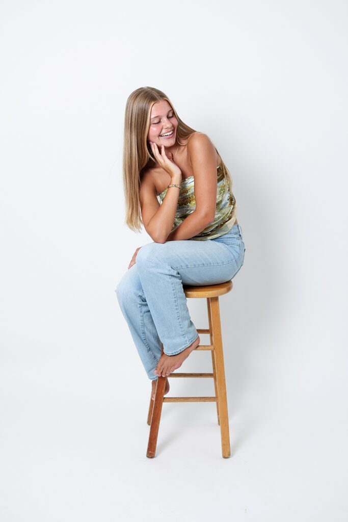 Playful senior portrait of laughing while sitting barefoot on a stool in a Malibu photo studio