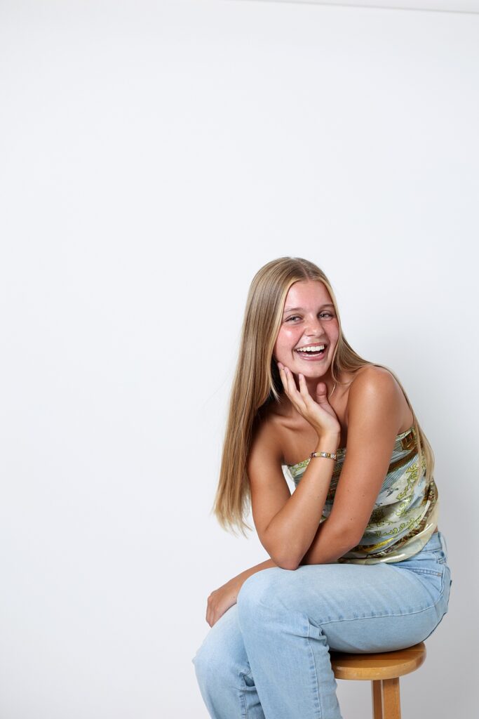 Candid Malibu senior portrait of laughing with her head tilted while sitting on a stool