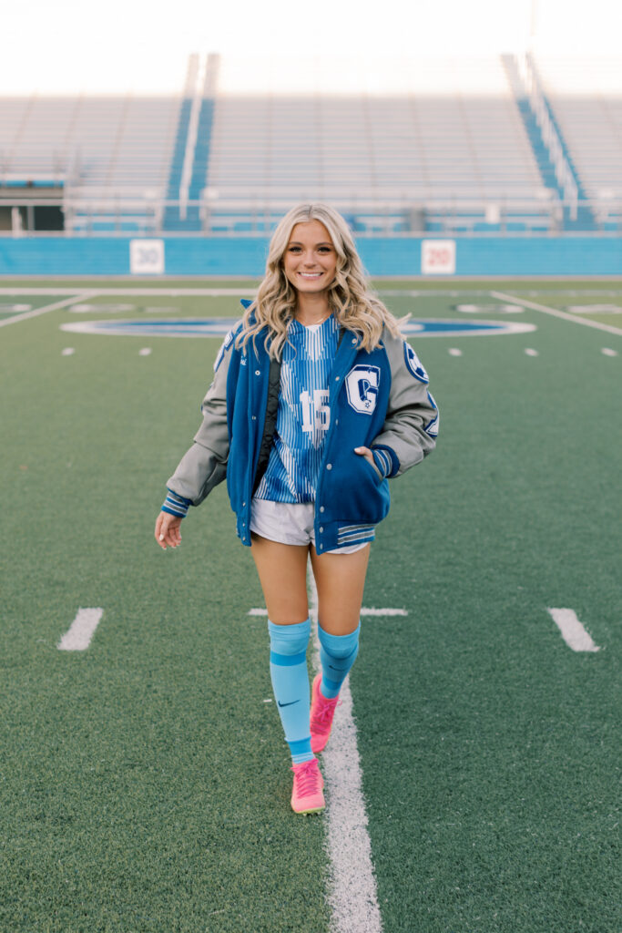 Senior girl smiling and walking across football field in varsity jacket, Malibu senior photographer