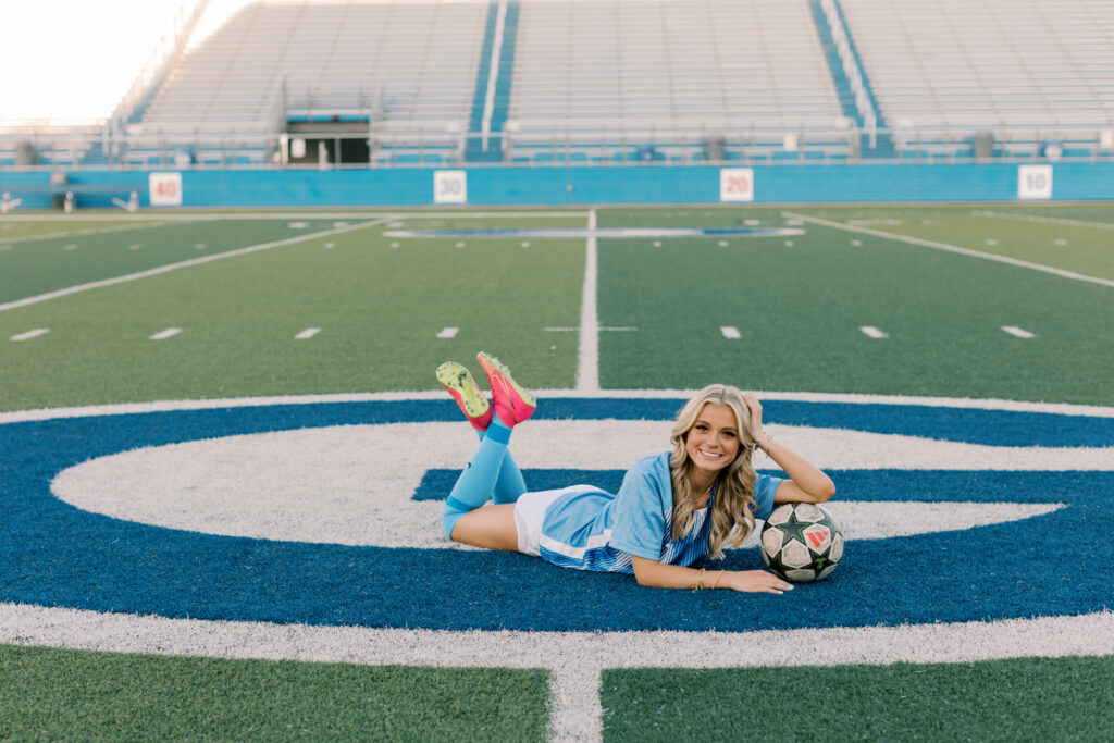 Blonde high school senior girl in class of 2025 letterman jacket laying on soccer field, Malibu senior photos