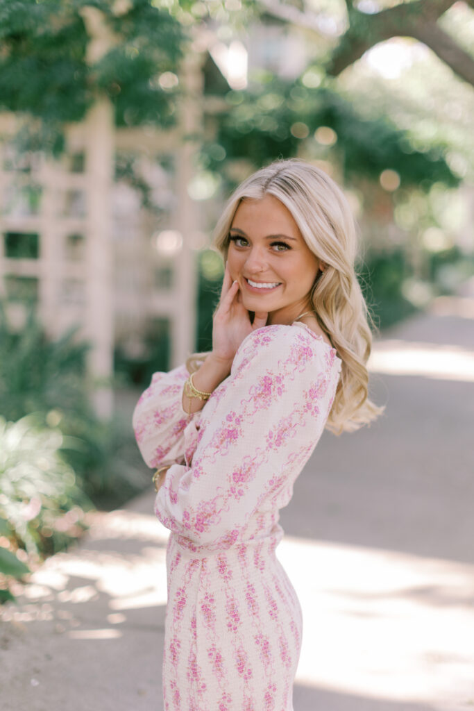 Close-up of smiling senior girl with soft glam makeup and bokeh greenery background