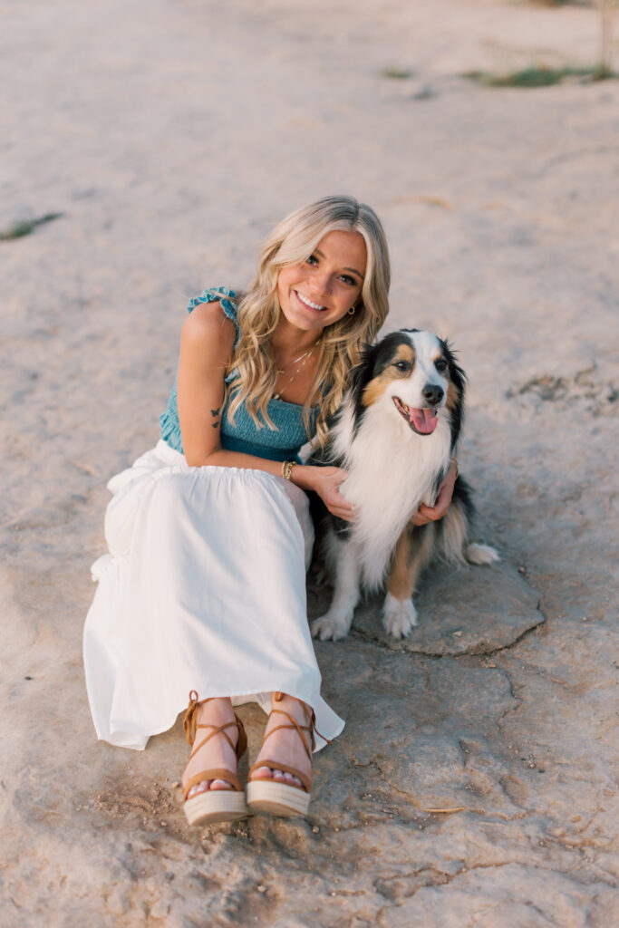 Senior girl sits with her dog on the rocks by a lake at sunset, showing their bond during her Southern California senior photos.