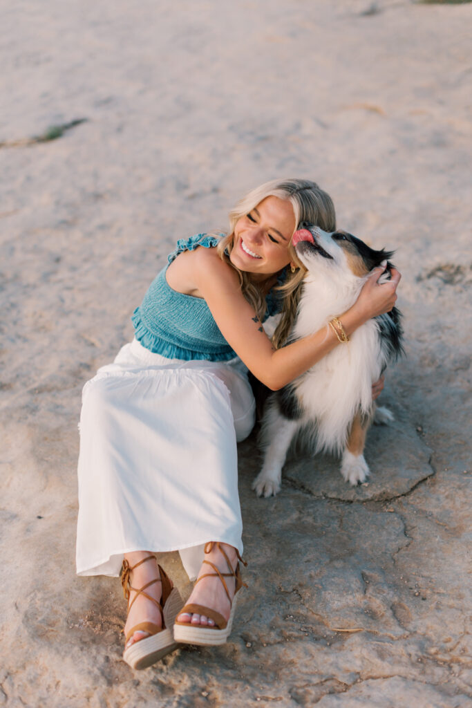 Candid moment of a dog giving a kiss to a senior girl during a fun lake photo session. Southern California senior photos with pets.