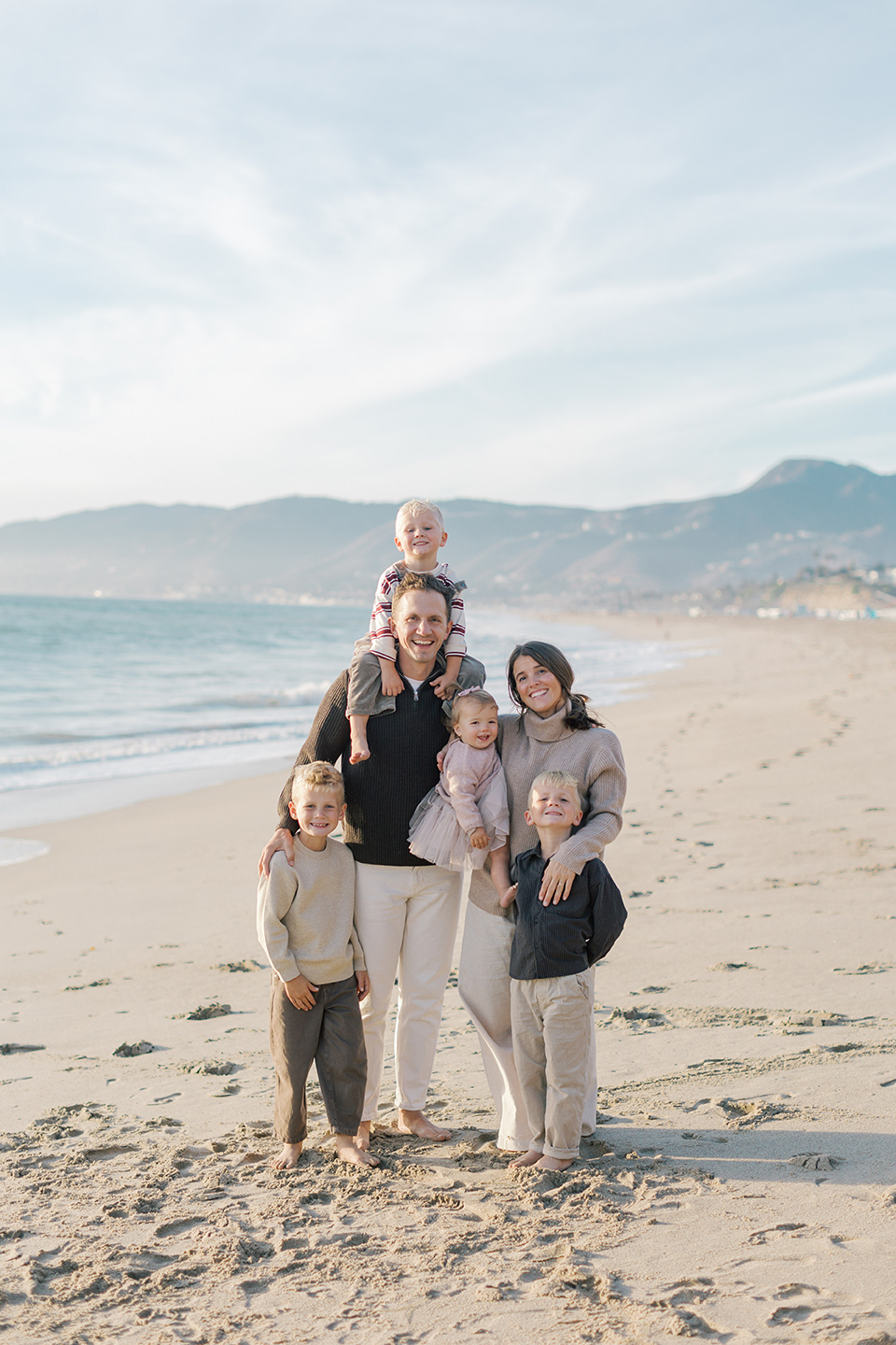Family standing together with the Malibu coastline behind them during golden hour at Westward Beach.