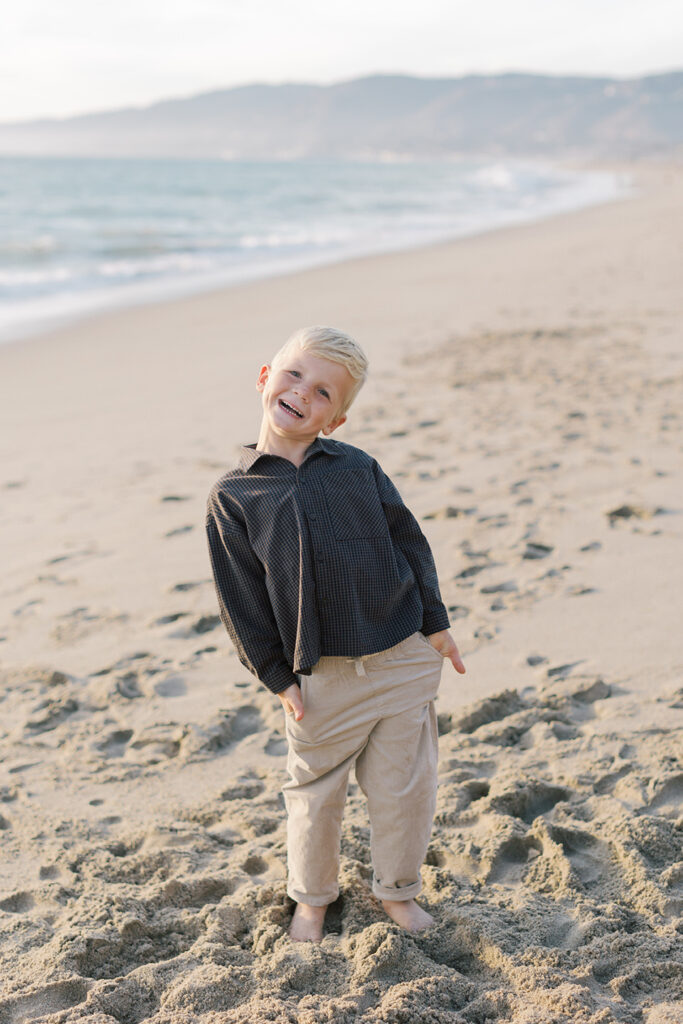Young boy smiling as he stands on the beach during a family session at Westward Beach in Malibu.