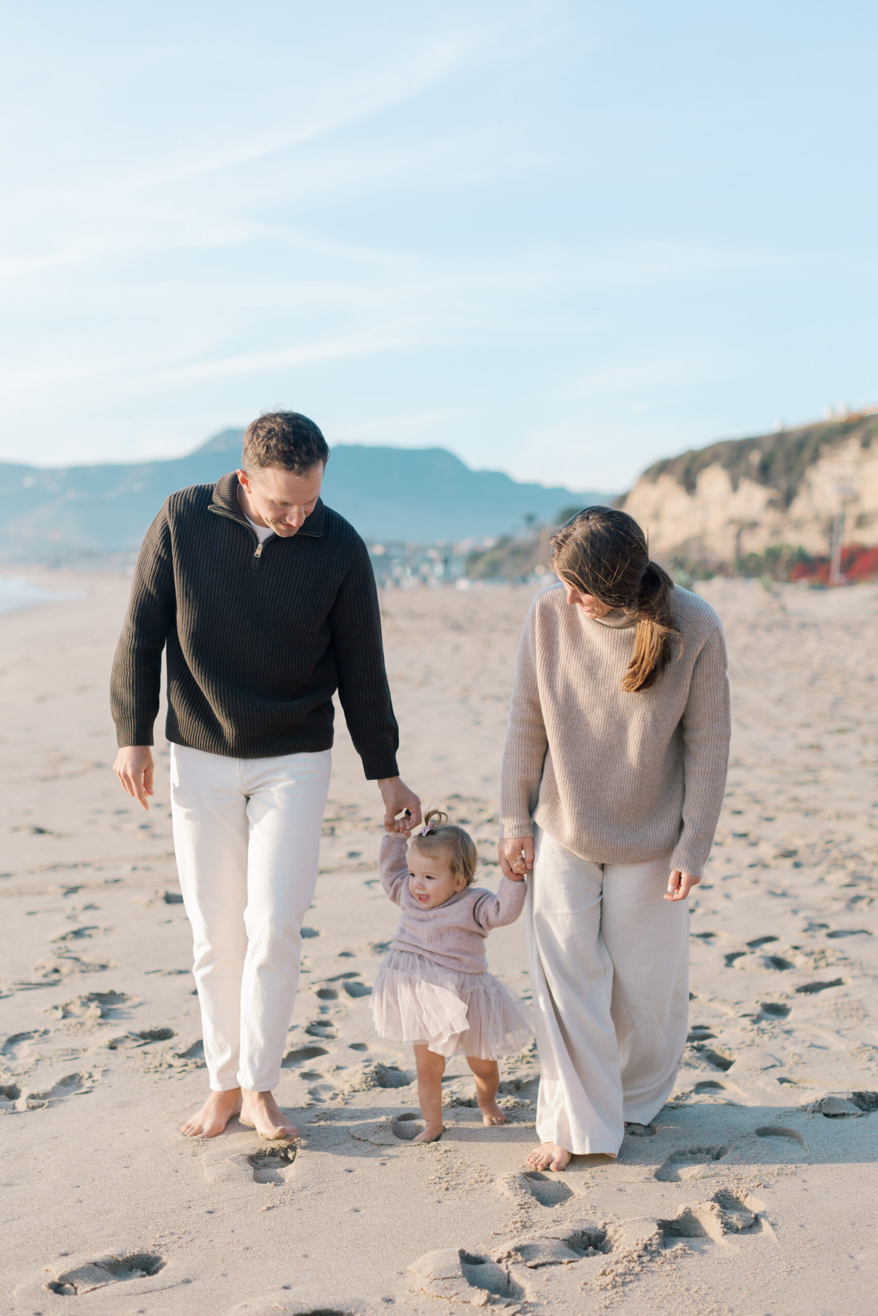 Parents walking hand-in-hand with their toddler along the sand at Westward Beach.