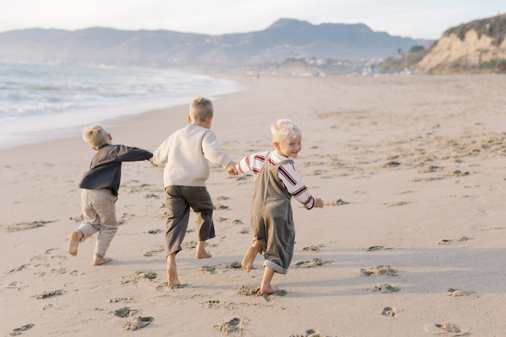 Children running along the sand in soft golden light during their Malibu family session.