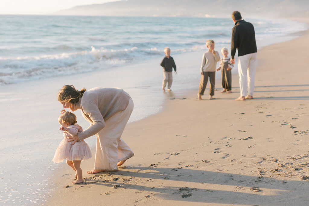 Parents walking with their children along the shoreline during a pastel Malibu sunset.
