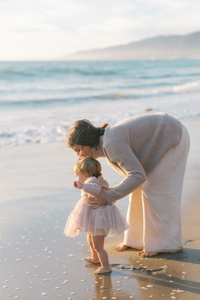 Mother walking along the shoreline while holding her baby during golden hour at Westward Beach.