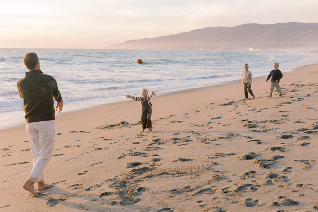 Candid photo of dad playing football with kids on Westward beach by Malibu family photographer.