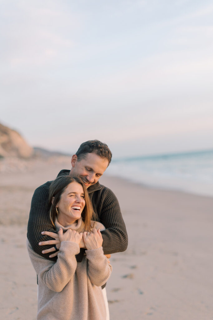 Couple embracing and laughing near the shoreline during golden hour during family photos at Westward Beach in Malibu.