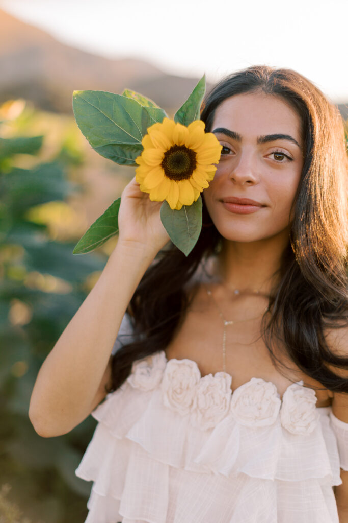 Close-up senior portrait holding a sunflower in a sunflower field near Westlake Village California