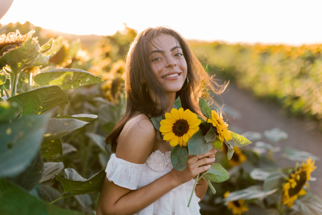 Smiling senior holding sunflowers during golden hour in a sunflower field near Westlake Village