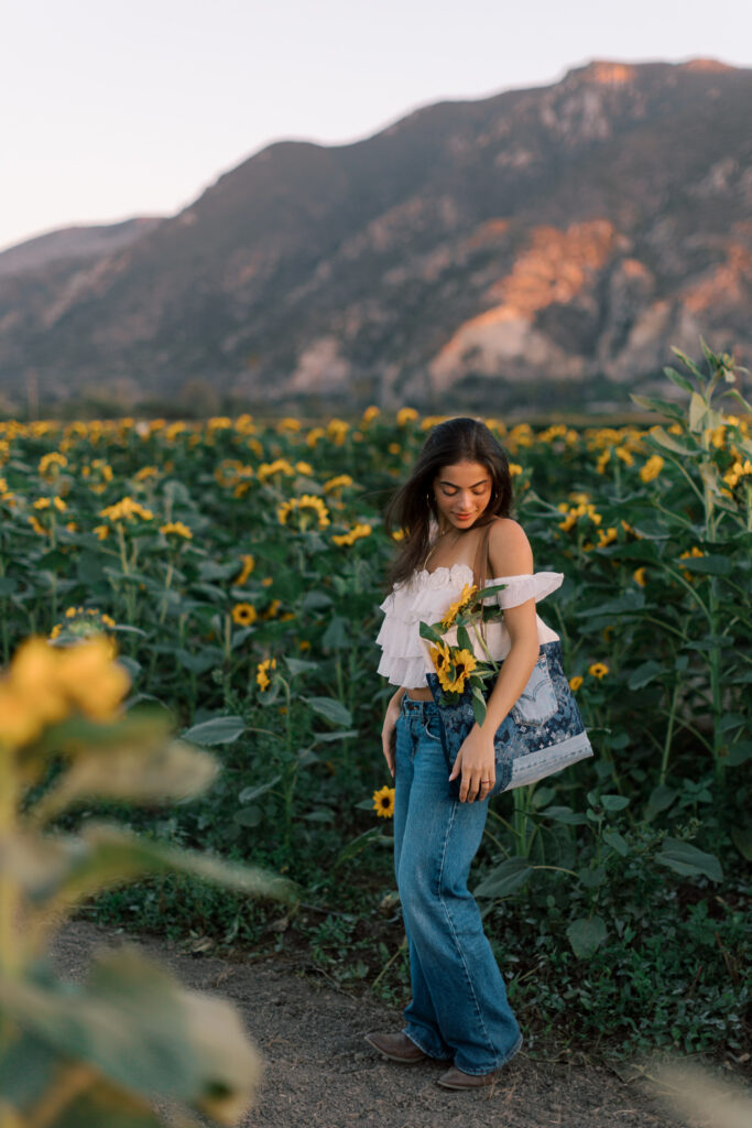 Wide senior portrait walking through a sunflower field near Thousand Oaks with mountains in the background