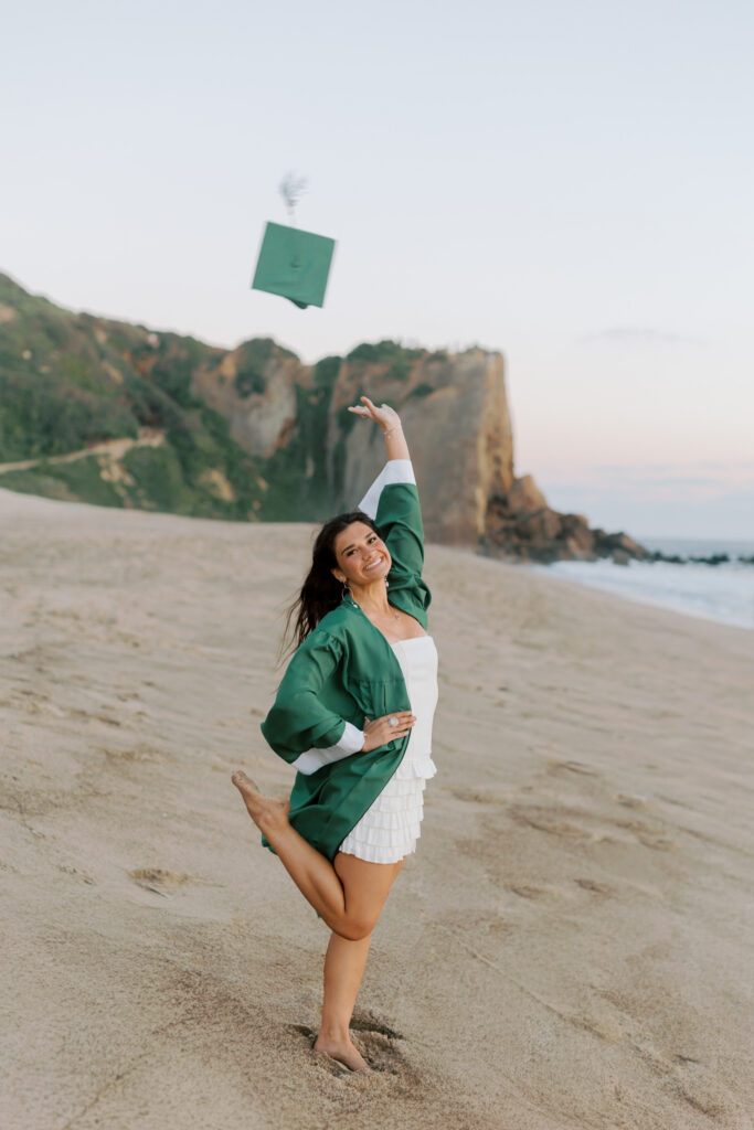 Thousand Oaks High School senior tossing graduation cap in the air at Point Dume Malibu beach with cliffs behind, cap and gown senior photos Southern California