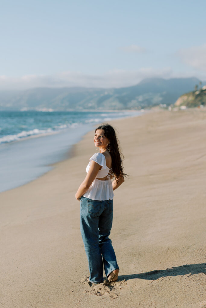 high school senior standing barefoot in the sand looking back at camera on Malibu beach, full body portrait Point Dume senior photographer