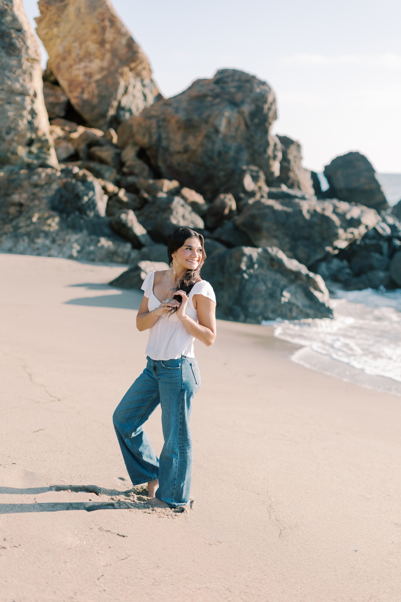 high school senior standing on sandy beach near large rocks at Point Dume in Malibu, natural light senior photos Southern California photographer
