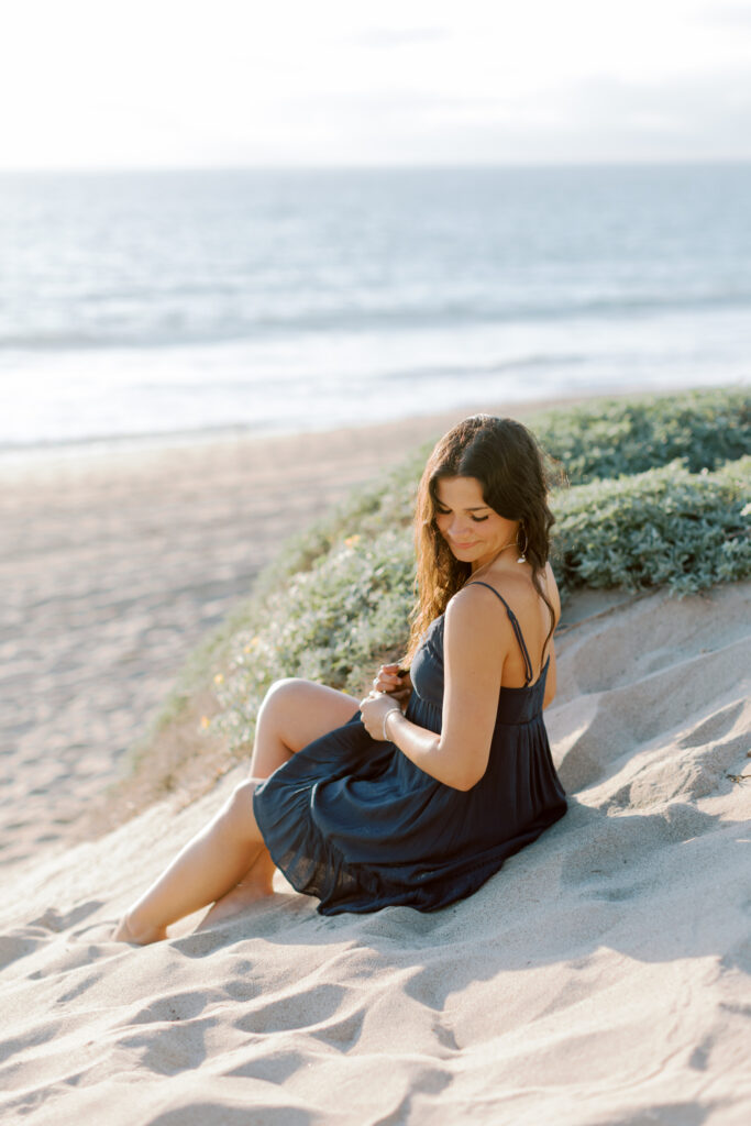 Thousand Oaks high school senior sitting in sand at Westward Beach Malibu looking back over shoulder, natural light beach senior photos