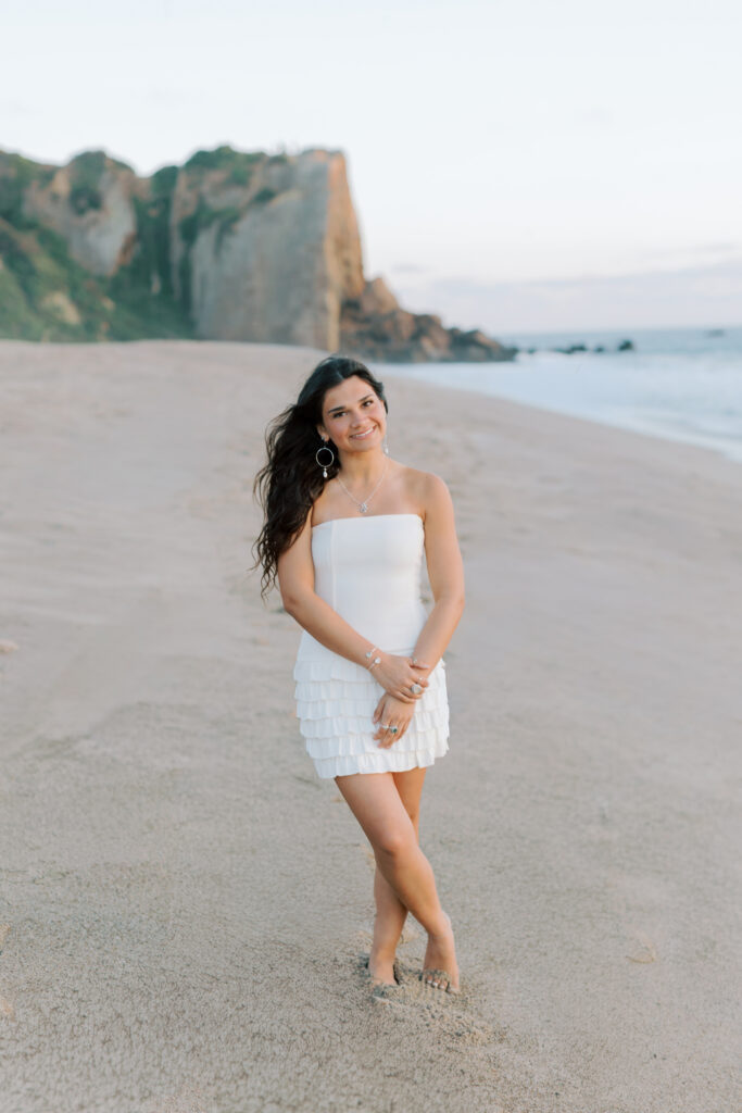 high school senior standing on beach at Point Dume Malibu with cliffs in background, full body portrait in white dress Thousand Oaks senior photographer
