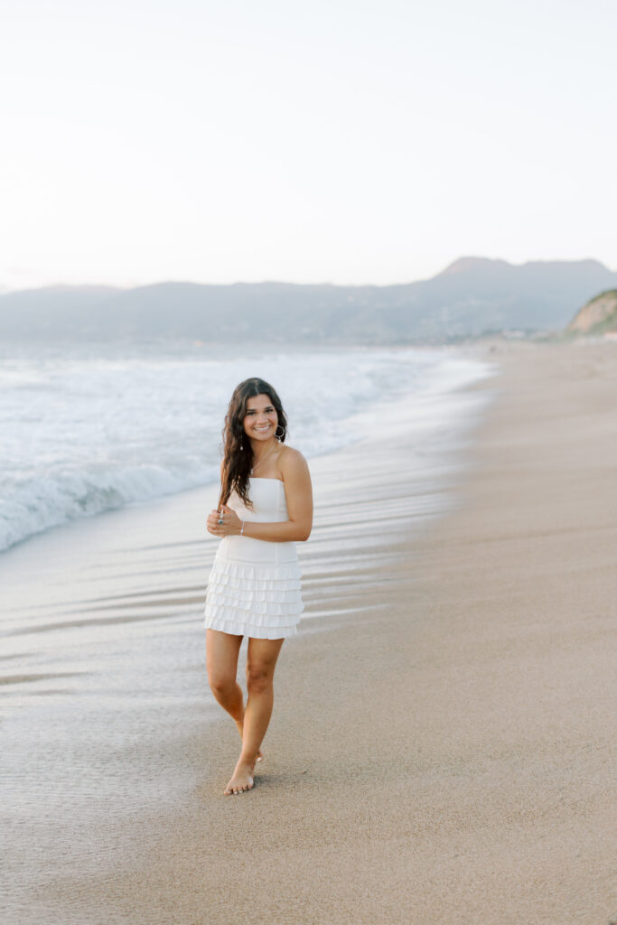 high school senior walking along shoreline at Westward Beach Malibu in white dress, full body beach senior photos Southern California