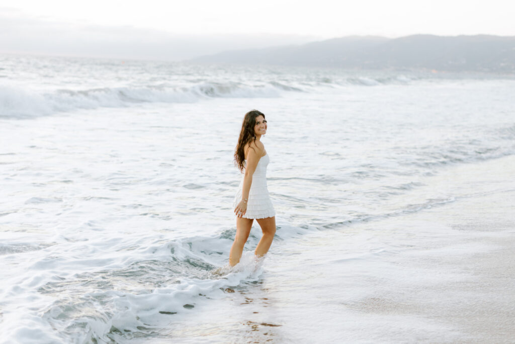 high school senior walking in ocean water at Westward Beach Malibu in white dress, candid beach senior photos Thousand Oaks photographer