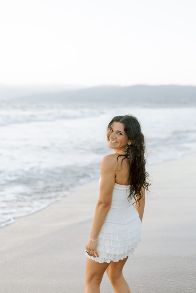 high school senior at Westward Beach Malibu looking back over shoulder in white dress near ocean, candid beach senior portrait Thousand Oaks photographer