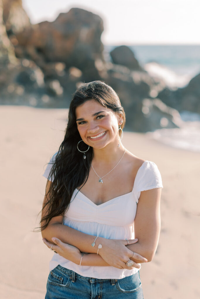 close up Malibu senior portrait of Thousand Oaks senior girl smiling in soft sunset light with beach and rocks blurred in the background