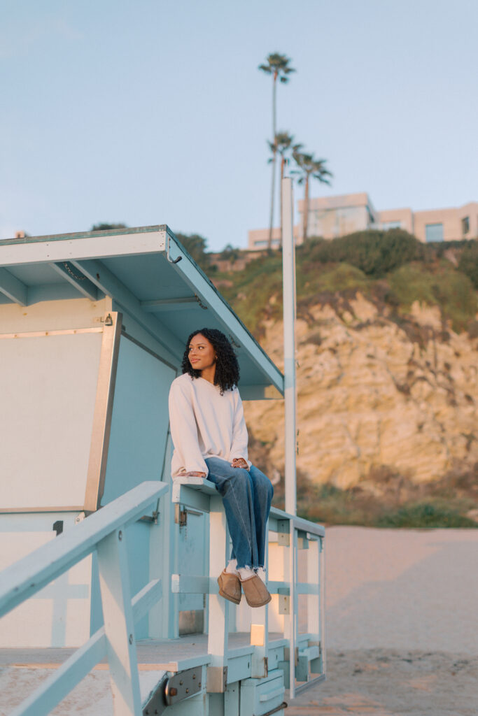 Oaks Christian senior sitting on a lifeguard stand at Point Dume Malibu with palm trees and cliffs behind