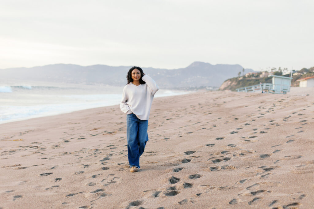 Malibu senior photos featuring Oaks Christian senior walking on the beach with ocean and mountains in the background