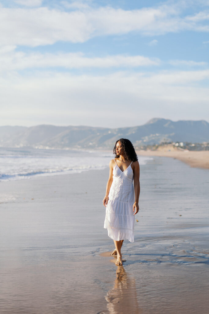 Oaks Christian senior walking along the shoreline at Westward Beach Malibu with mountains and ocean in the background