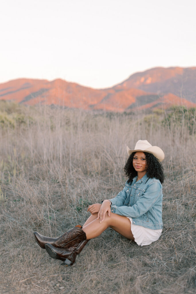 Thousand Oaks High School senior sitting in a dry field with mountains behind her in Southern California during golden hour