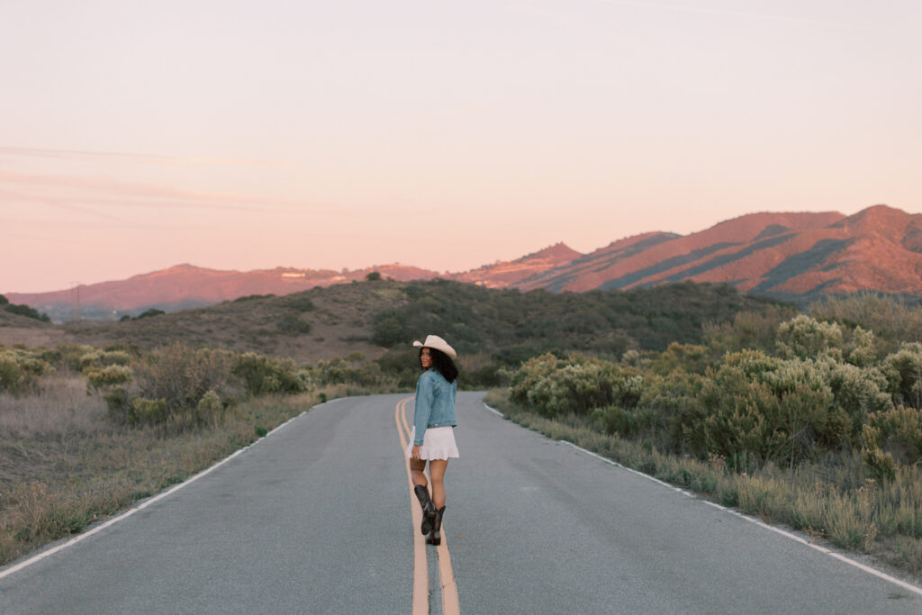 Thousand Oaks senior standing on a winding road in the Santa Monica Mountains with glowing sunset hills in the background
