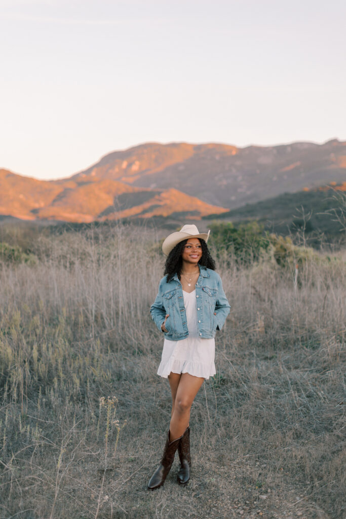 Full body portrait of a Thousand Oaks High School senior standing in a rural field with mountains in Southern California